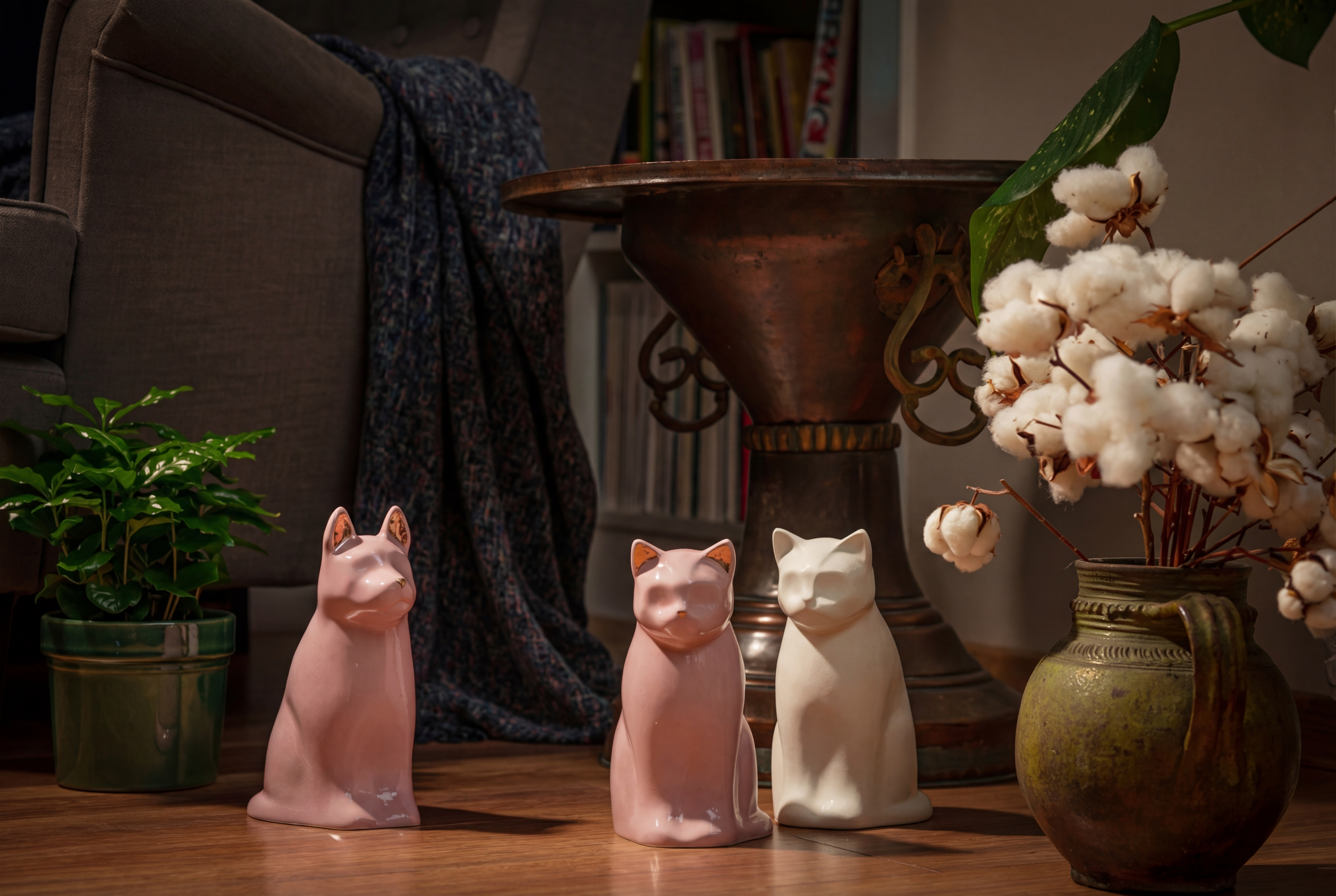 Tre keramiske katt-urne på tregulv med planter og interiør.